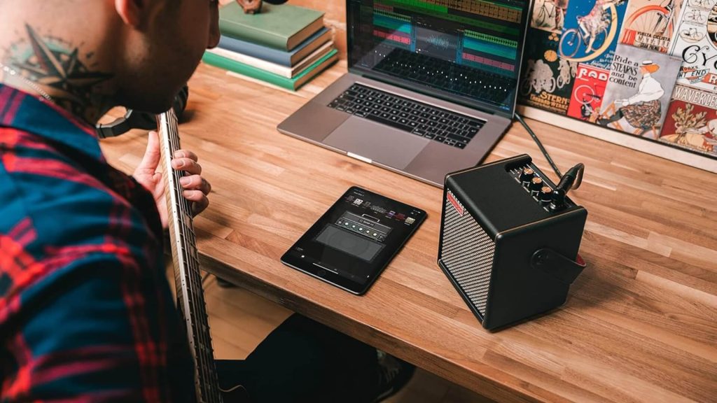 Guitarist practicing at desk with Positive Grid Spark Mini amp and laptop home studio setup